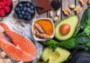 Anti-inflammatory foods like salmon, turmeric, avocado, berries, nuts, and leafy greens arranged on a wooden table.